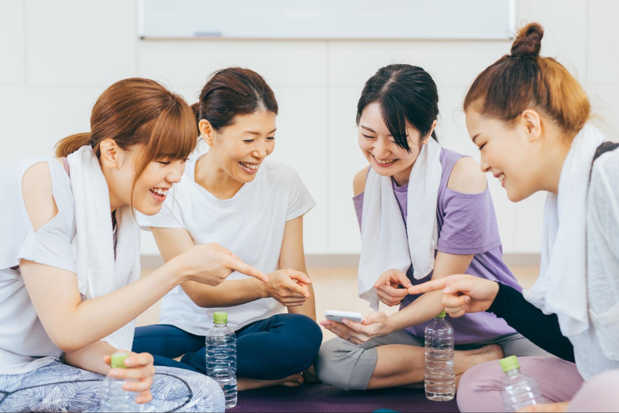 スポーツジムでスマホを見て談笑する女性たち