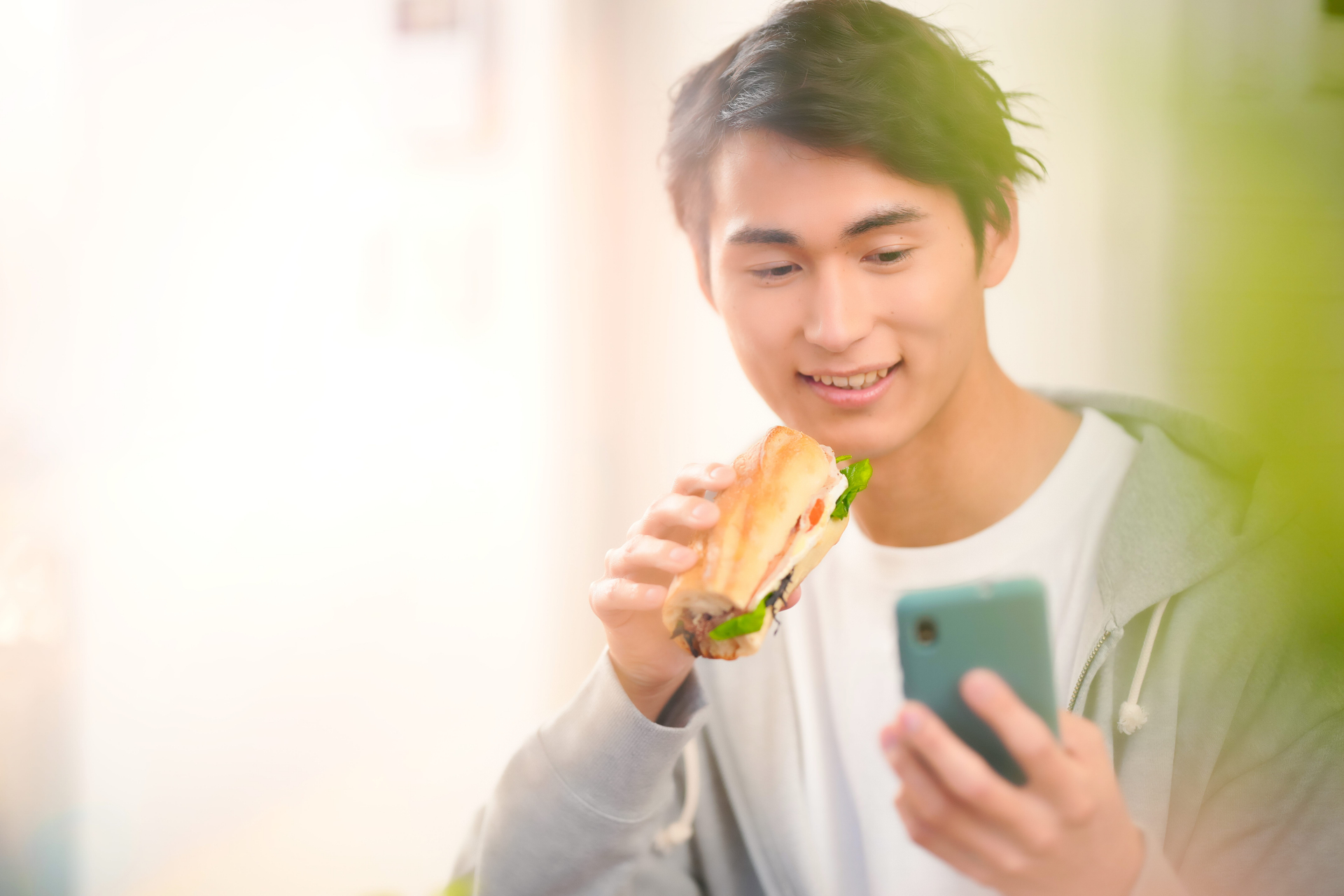 サンドイッチを食べながらスマホを見ている男性