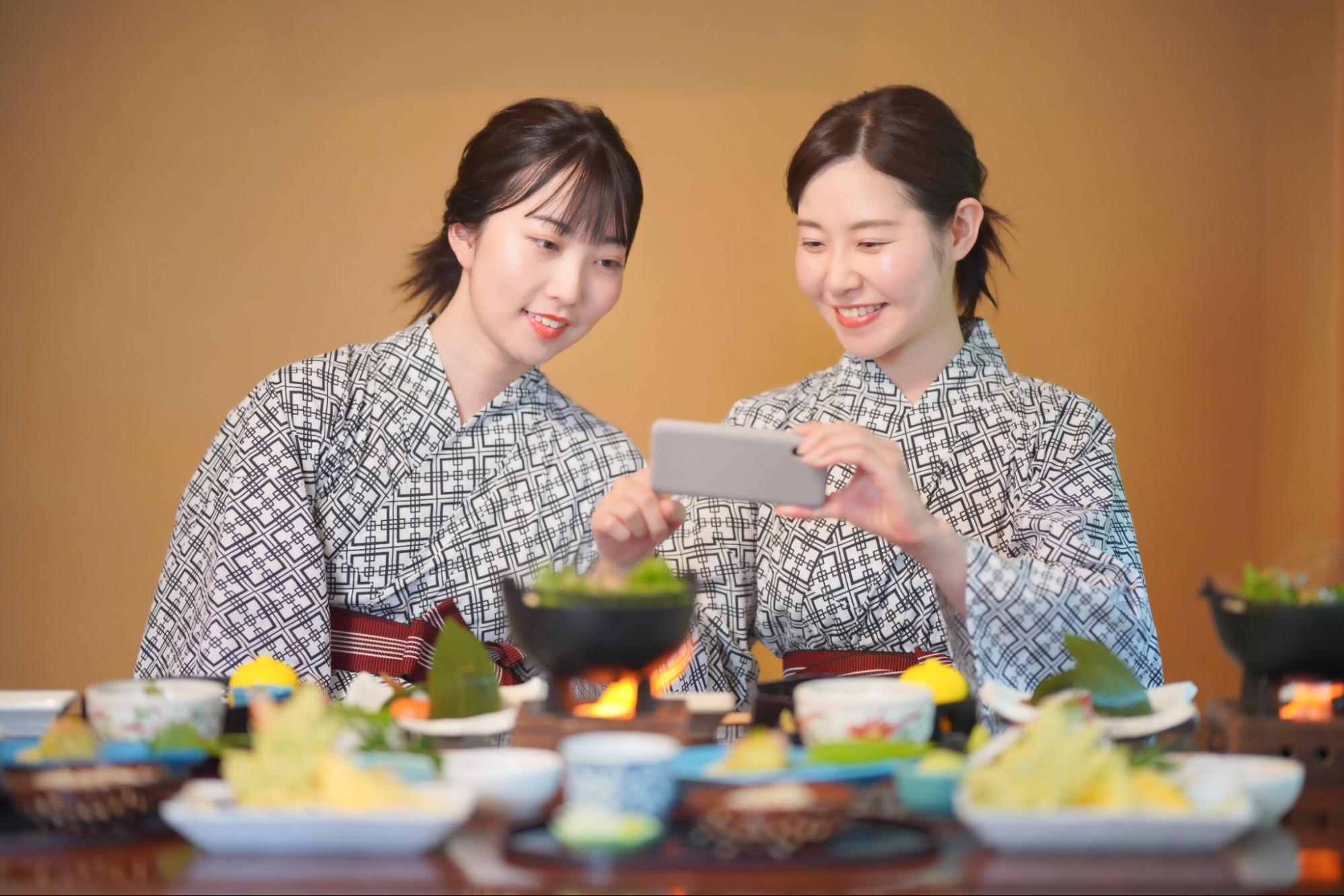 旅館の食事の写真を撮る2人の浴衣姿の女性