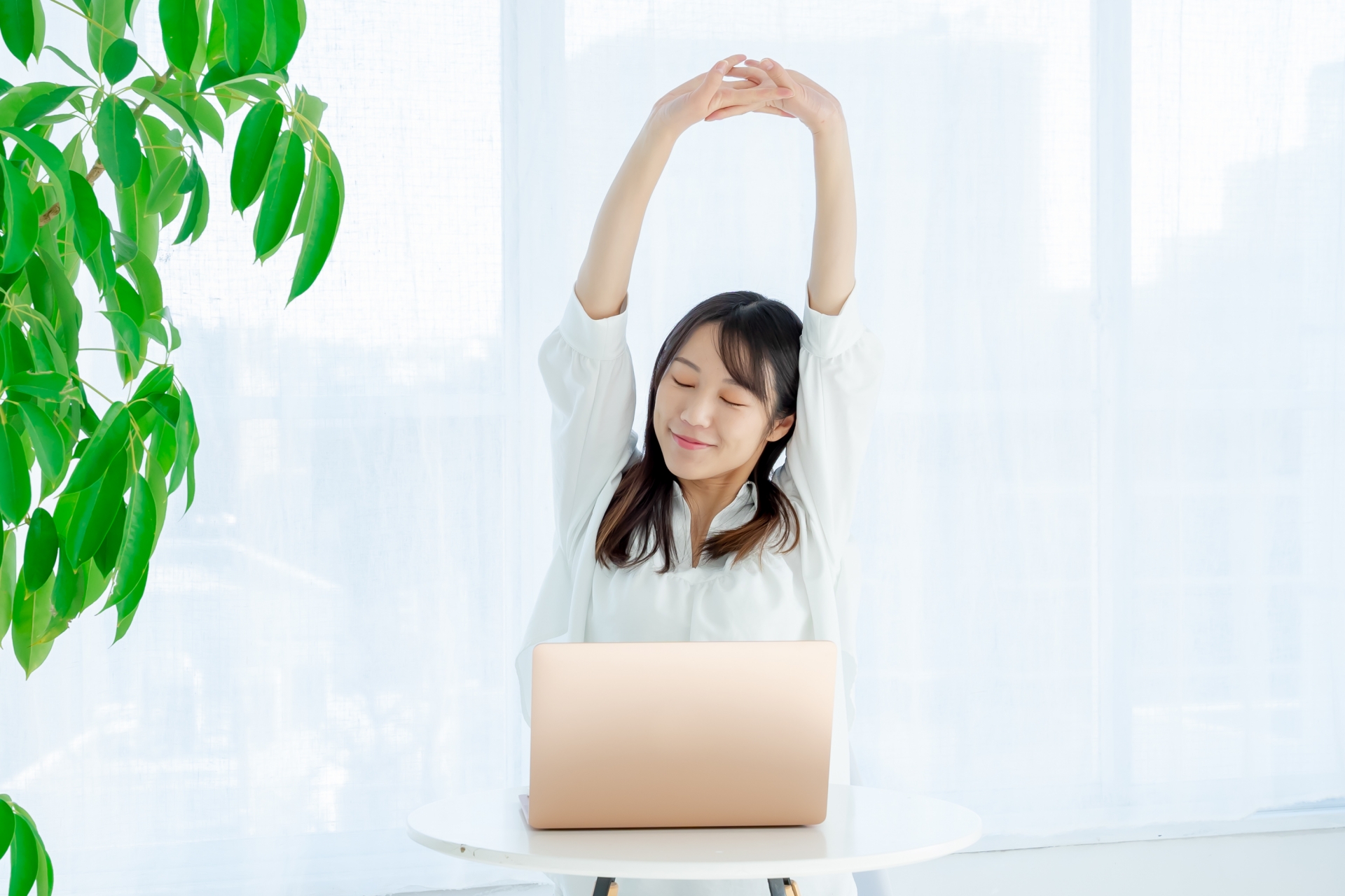ノートパソコンと伸びをして休憩する女性